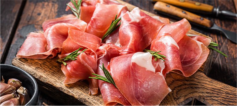 Jamon Serrano on a wooden board, garnished with rosemary.